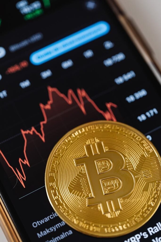 pexels-photo-5980863 Gold Bitcoin coin on a smartphone showing financial graph, symbolizing digital currency and blockchain trends.